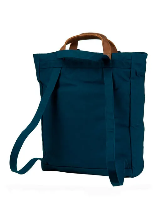 Vista trasera de una mochila para viajar de lona azul oscuro con asas de cuero marrón, aislada sobre fondo blanco.