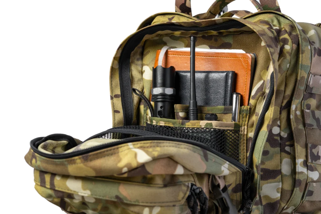 Primer plano de mochilas de rescate tipo tácticas de camuflaje abiertas con su equipo: radio, linterna y libretas.