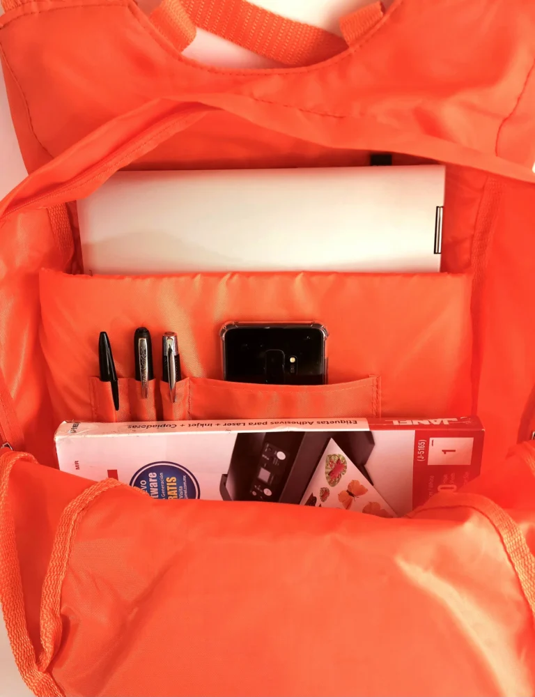 An orange school backpacks interior showing a laptop pens a smartphone and a book clearly organized in multiple pockets